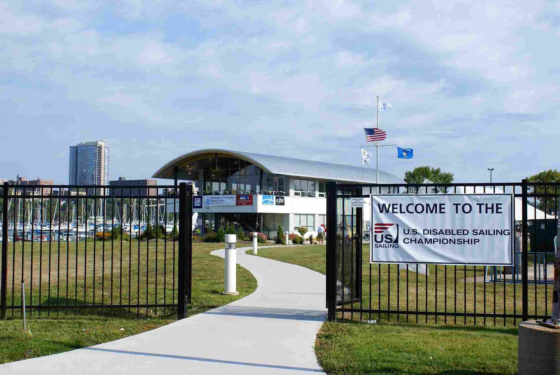 Welcome sign at iron gate for the U.S. Disabled Sailing Championships with MCSC Building and Milwaukee in the background