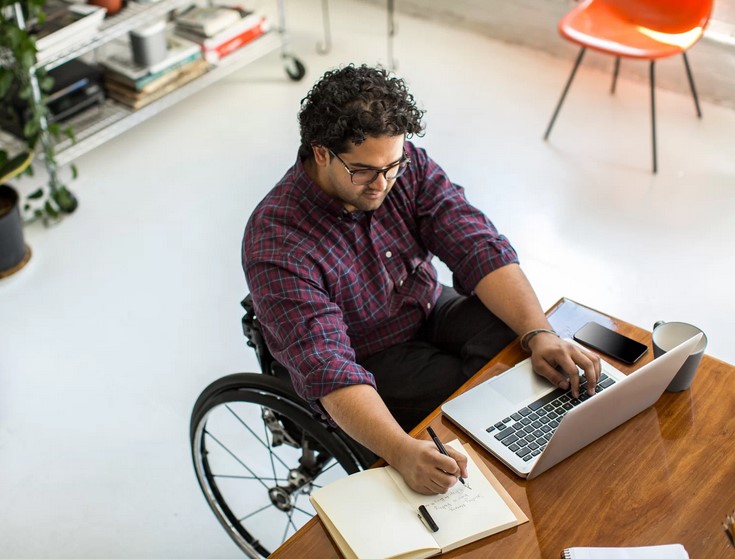 photo of a young man in a wheelchair at a work desk in an office