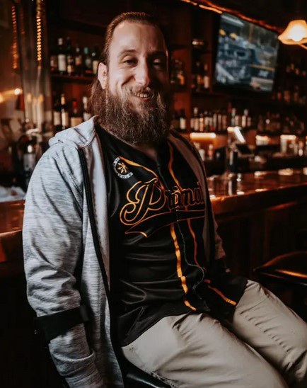 Color photograph of a handsome, middle aged ma in a bar with a baseball joursey on